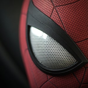 Puede incluir: Primer plano de una m&aacute;scara de Spider-Man roja y negra con una pieza de ojo de malla blanca.