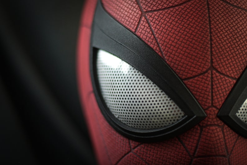 Puede incluir: Primer plano de una m&aacute;scara de Spider-Man roja y negra con una pieza de ojo de malla blanca.