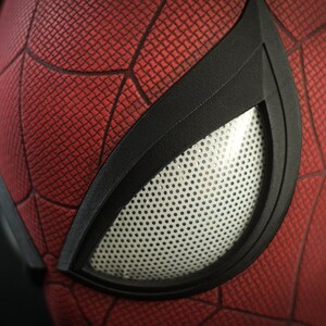 Puede incluir: Primer plano de una m&aacute;scara de Spider-Man roja y negra con una abertura para los ojos de malla blanca.