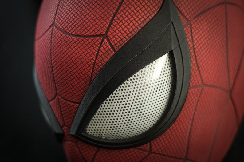 Puede incluir: Primer plano de una m&aacute;scara de Spider-Man roja y negra con una abertura para los ojos de malla blanca.