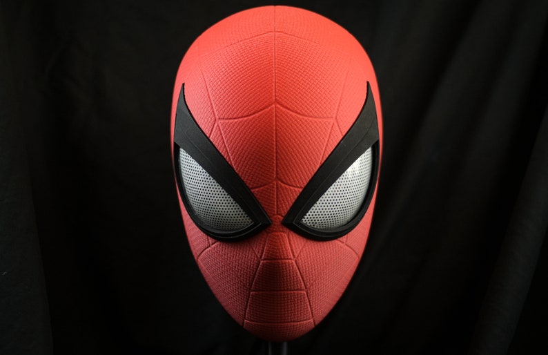 Puede incluir: Una m&aacute;scara de Spider-Man roja y negra con una superficie texturizada y un dise&ntilde;o de ojo de malla.