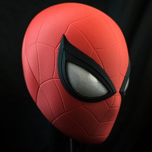Puede incluir: Una m&aacute;scara de Spider-Man roja y negra con una superficie texturizada y una pieza de ojo de malla.
