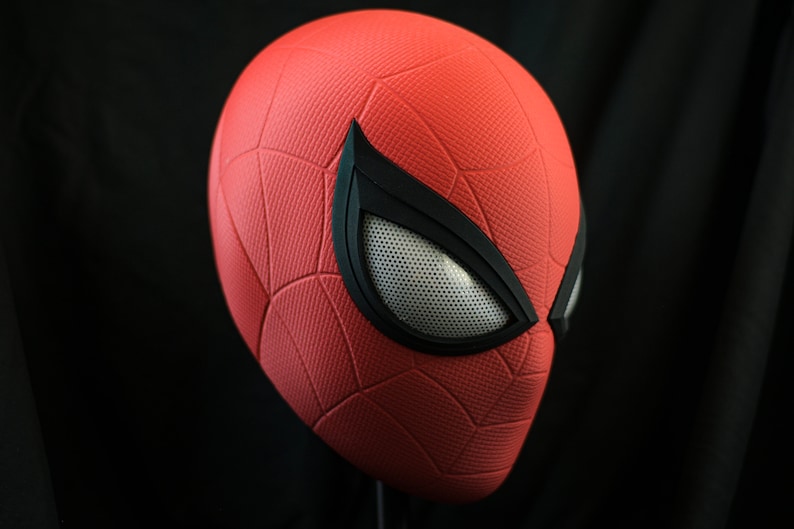 Puede incluir: Una m&aacute;scara de Spider-Man roja y negra con una superficie texturizada y una pieza de ojo de malla.
