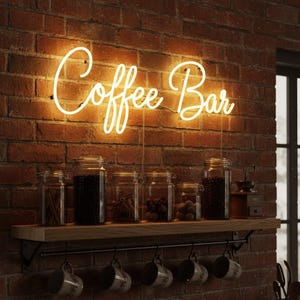 Può includere: Un'insegna al neon "Coffee Bar" è montata su un muro di mattoni. Sotto, una mensola in legno con barattoli di vetro pieni di chicchi di caffè e spezie. Sotto, tazze appese a una barra di metallo.