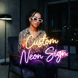 May include: A neon sign with the words "Custom Neon Sign" in a script font. The top portion glows yellow, and the bottom glows purple. The sign is held by a person wearing a snakeskin print shirt and white sunglasses.