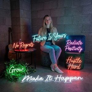 May include: A woman sits with several neon signs with motivational phrases. The signs include "Future Is Yours", "No Regrets", "Radiate Positivity", "Hustle Hard", "Grow", and "Make It Happen". The signs are in various colors.