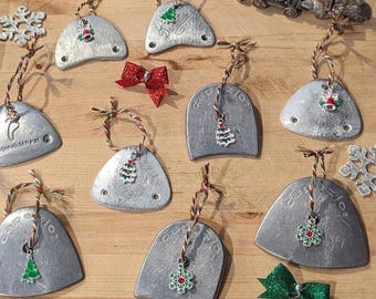 Peut inclure: Une collection d'ornements en métal argenté en forme de triangles arrondis, chacun doté de deux trous et d'une ficelle avec une petite breloque festive. Les breloques incluent des sapins, des flocons et des cloches. Deux nœuds pailletés sont inclus.