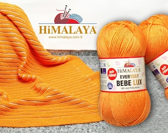 May include: Two orange skeins of Himalaya Everyday Bebe Lux yarn. The yarn is 100% anti-pilling acrylic. A knitted orange and white striped blanket is in the background.