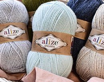 Puede incluir: Seis ovillos de hilo en varios colores, incluyendo verde, azul, beige y azul claro. El hilo está etiquetado como "alize" y está dispuesto en una cesta.