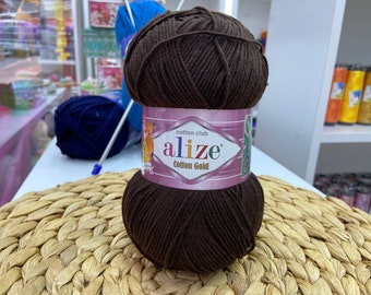 May include: A brown ball of yarn labeled "cotton club alize Cotton Gold" on a woven straw mat.