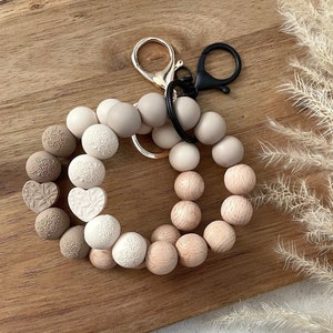 Peut inclure: Un porte-clés en silicone beige et marron avec un anneau de clé doré et noir. Les perles ont un motif de cœur et de fleurs.