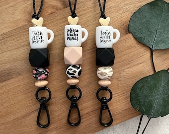 Pode incluir: Três cordões pretos com pingentes de coração dourado e canecas de café de cerâmica branca com texto preto. Cada cordão tem uma conta com padrão preto e branco, uma conta preta, uma conta bege e uma conta com padrão branco e marrom. Os cordões terminam com um clipe de metal preto. As canecas dizem "Teach Love Inspire", "Coffee Teach Repeat" e "Teach Love Inspire".