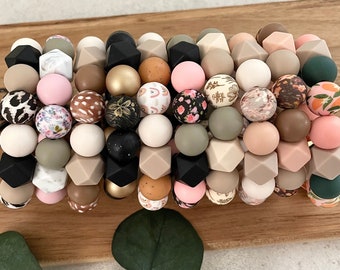 May include: A colorful silicone bead bracelet with various patterns and colors, including pink, brown, green, and black. The beads are arranged in a circular pattern and have a variety of textures.