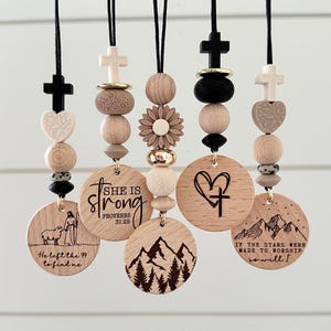 May include: Wooden pendants with inspirational quotes and religious symbols. Each pendant features a unique design, including crosses, hearts, and mountain scenes. The text includes "She is strong" and "He left the 99 to find me."