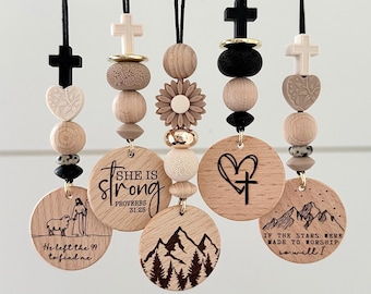 May include: Wooden pendants with inspirational quotes and religious symbols. Each pendant features a unique design, including crosses, hearts, and mountain scenes. The text includes "She is strong" and "He left the 99 to find me."