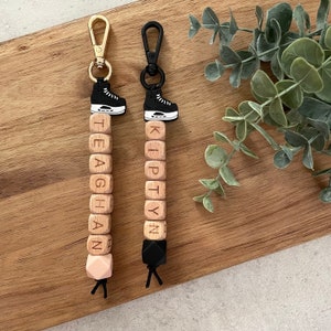 May include: Two wooden bead keychains with the names Teaghan and Kiptyn spelled out on the beads. Each keychain has a black and white ice skate charm at the top.