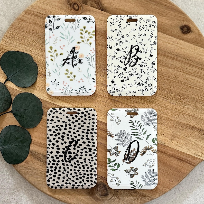 Puede incluir: Cuatro etiquetas de equipaje rectangulares con diferentes patrones y letras. Una etiqueta tiene un dise&ntilde;o floral con la letra "A", otra tiene un patr&oacute;n floral en blanco y negro con la letra "B", una tercera tiene un patr&oacute;n de lunares en blanco y negro con la letra "C", y la &uacute;ltima tiene un dise&ntilde;o floral con la letra "D".