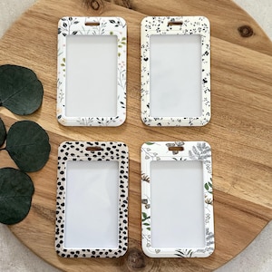 Puede incluir: Cuatro porta credenciales de pl&aacute;stico transparente con estampados florales y de lunares. Los soportes tienen forma rectangular con esquinas redondeadas y una ranura para un cord&oacute;n. Los estampados incluyen fondos blancos con dise&ntilde;os florales negros y verdes y un dise&ntilde;o de lunares en blanco y negro.