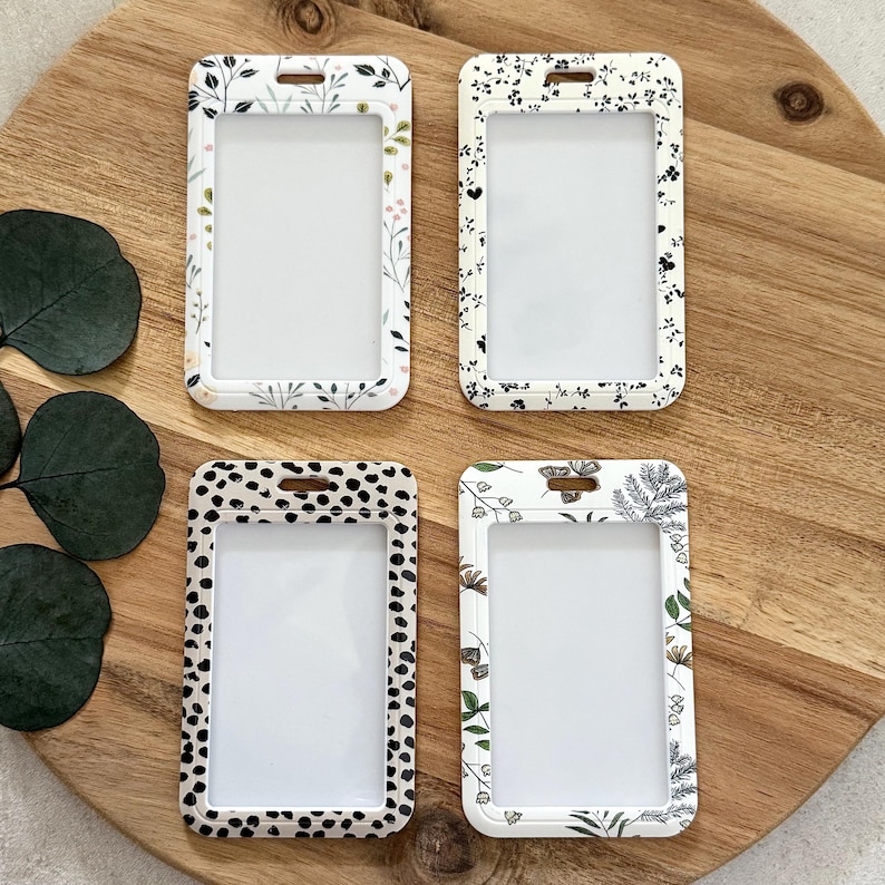 Puede incluir: Cuatro porta credenciales de pl&aacute;stico transparente con estampados florales y de lunares. Los soportes tienen forma rectangular con esquinas redondeadas y una ranura para un cord&oacute;n. Los estampados incluyen fondos blancos con dise&ntilde;os florales negros y verdes y un dise&ntilde;o de lunares en blanco y negro.