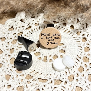 May include: A circular light wood car air freshener clip featuring the black engraved text "DRIVE SAFE I LOVE YOU, MAL ♡ JASON". The set includes a black plastic vent clip attachment and two small white round absorbent refill pads.