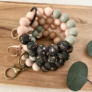 May include: A black, green and pink beaded keyring with a floral pattern. The keyring has a metal ring and two metal clasps.