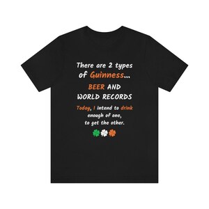 K&ouml;nnte beinhalten: Schwarzes T-Shirt mit wei&szlig;em Text, der lautet: "There are 2 types of Guinness... BEER AND WORLD RECORDS. Today, I intend to drink enough of one, to get the other." Unter dem Text befinden sich vier gr&uuml;ne Kleebl&auml;tter mit orangefarbenen Zentren.