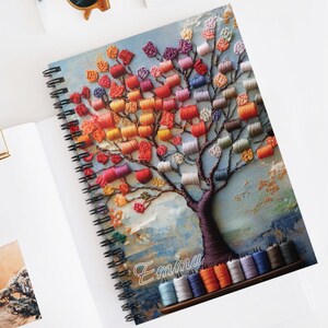 May include: A spiral bound notebook with a colorful embroidered tree design. The tree is made of colorful thread spools and the notebook is personalized with the name "Emma".