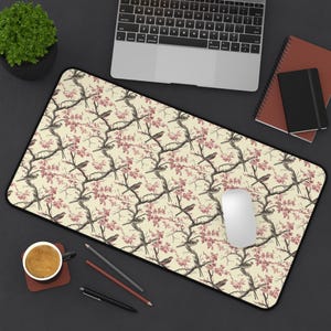 May include: A cream-coloured desk mat with a repeating pattern of pink flowers and brown birds. The mat has a black border.
