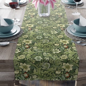 May include: A green table runner with a floral pattern featuring white flowers and green leaves. The runner is on a wooden table with two place settings.