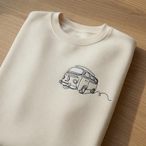 Könnte beinhalten: Ein cremefarbenes Sweatshirt mit Rundhalsausschnitt und einer schwarzen, einzeiligen Stickerei eines Vintage-Campingbusses auf der linken Brust. Die minimalistische Linienzeichnung zeigt die Silhouette des Fahrzeugs mit Fenstern und Rädern.