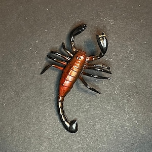May include: A brown and black scorpion figurine with a curled tail. The scorpion is posed with its legs outstretched and its stinger raised.