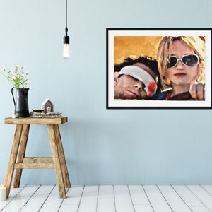 K&ouml;nnte beinhalten: Ein Schwarz-Wei&szlig;-Druck in einem schwarzen Rahmen, der ein Paar in einem Auto zeigt. Die Frau tr&auml;gt eine Sonnenbrille und der Mann hat ein Bandage &uuml;ber den Augen. Der Hintergrund ist ein verschwommenes Bild eines gelben und orangen Sonnenuntergangs.