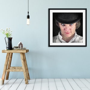K&ouml;nnte beinhalten: Ein gerahmtes Schwarzwei&szlig;portr&auml;t einer Person, die einen schwarzen Bowlerhut und ein wei&szlig;es Hemd tr&auml;gt. Die Person hat dunkles Haar und blaue Augen. Der Hintergrund ist schwarz.