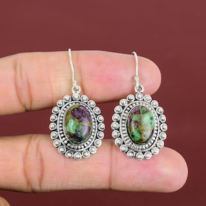 May include: Silver earrings with a green and purple oval gemstone set in a silver bezel. The earrings have a beaded border around the gemstone.