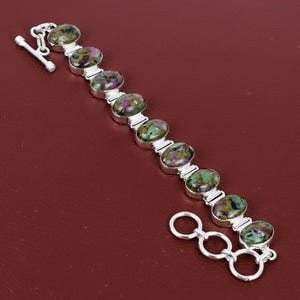 Puede incluir: Una pulsera de plata con piedras preciosas ovaladas en tonos verdes y morados. Las piedras están engastadas en biseles individuales de plata y conectadas por eslabones de plata. La pulsera tiene un cierre de palanca. Mide unos 19 cm.