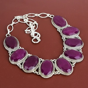 Könnte beinhalten: Eine silberne Halskette mit einer Kette und sieben großen ovalen, violetten Edelsteinen. Die Edelsteine sind in silbernen Fassungen mit dekorativen Details gefasst.