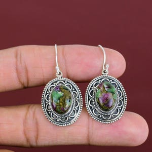 Puede incluir: Un par de pendientes de plata con piedras ovaladas verdes y rosas engastadas en marcos de plata ornamentados.