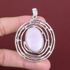 May include: A silver pendant featuring a swirling design and a light purple oval gemstone in the centre.
