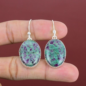 Peut inclure: Une paire de boucles d'oreilles en argent avec des pierres précieuses ovales de couleur verte et violette. Les boucles d'oreilles ont un design simple et sont parfaites pour un usage quotidien.