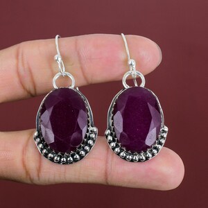 May include: A pair of silver earrings with a purple gemstone in an oval shape. The earrings have a beaded border around the gemstone.