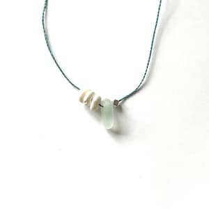 May include: A simple necklace with a light blue cord and three white shell beads and a light blue glass bead.