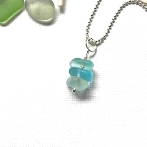 May include: A silver chain necklace with a pendant made of three stacked pieces of sea glass. The sea glass is a light blue color, with the top piece being the lightest and the bottom piece being the darkest.