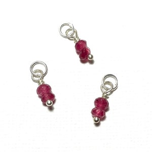 May include: Three silver charms with two red gemstone beads on each. The charms have a loop at the top for attaching to a bracelet or necklace.