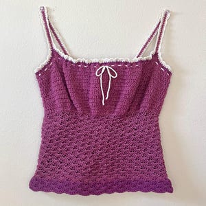 May include: A purple crochet tank top with white trim and a white bow at the neckline.