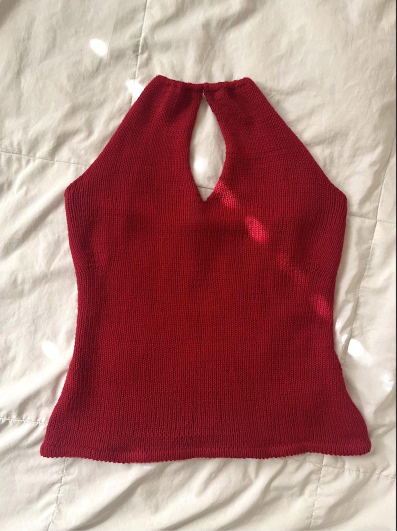 May include: A solid red halter top made of knitted fabric. The top has a keyhole detail at the neckline and a fitted silhouette. The garment is displayed on a white surface.