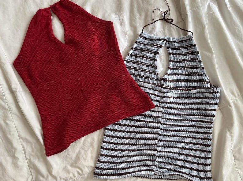 May include: Two knitted halter tops. One is solid red, the other is light blue with brown horizontal stripes. Both tops have a keyhole neckline and are made of a soft, textured knit fabric. The tops are displayed on a white surface.