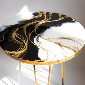 May include: Round black and white epoxy resin table top with gold swirls and a gold metal base with three legs.