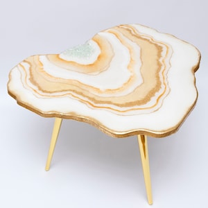 May include: A white and gold resin coffee table with a unique, organic shape and gold metal legs.