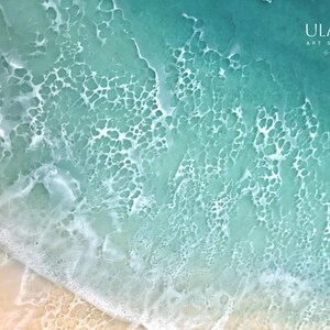 May include: Abstract painting of a turquoise ocean with white foam waves. The painting has a textured surface and a light blue and white color scheme.