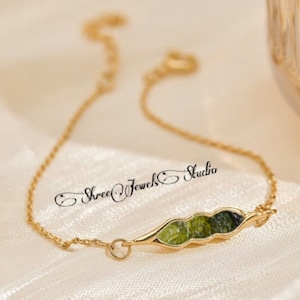 May include: A delicate gold bracelet with a pea pod design. The pod is filled with green and dark green stones. The bracelet is from Shree Jewel Studio.